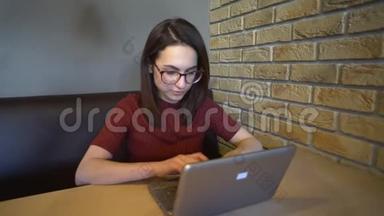 一个年轻的女人带着笔记本电脑坐在桌子旁。 一个女人拿着一台小笔记本电脑坐在家里写字