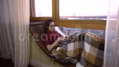 一个年轻的女人正在笔记本电脑上打字。 一个女孩躺在窗边的窗台上，手里拿着一台笔记本电脑。 在外面