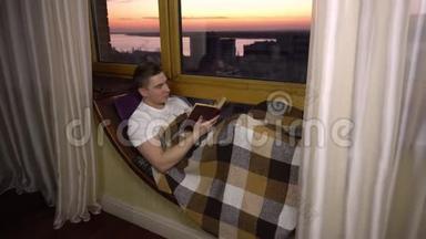 一个年轻人正在看书。 一个人躺在<strong>窗边</strong>的<strong>窗</strong>台上，手里拿着一本书。 晚上出去