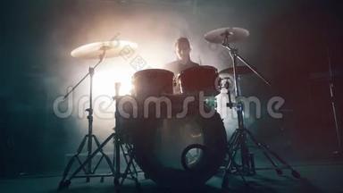 黑暗工作室里有一个男人在排练鼓声。 鼓组，鼓包在黑暗中，鼓手演奏音乐会。