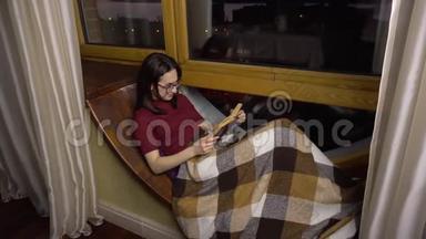 一个年轻的女人<strong>正在看书</strong>。 一个女孩躺在窗边的窗台上，手里拿着一本书。 晚上出去