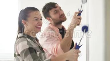 年轻夫妇装饰他们的新公寓。 年轻的夫妻正在粉刷墙壁。 一对漂亮的夫妇正在修理