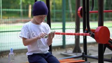 一个在街头公共健身器材上的<strong>男孩</strong>看着他的智能手机