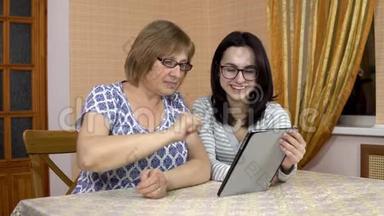 女儿教妈妈如何使用药片。 一个年轻的女人告诉她的老母亲在哪里点击平板电脑。 家庭