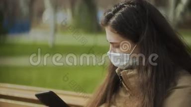 年轻女子戴着防护面具，在城市公园使用智能手机进行语音留言。 大流行Covid-19冠状病毒