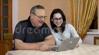 一个女儿和她父亲通过笔记本电脑通过视频交流与朋友交流。 一个年轻的女人和一个老的
