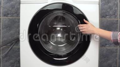 一个年轻的女人用洗衣机装衣服。 一个女人打开洗衣机，把衣服放进去然后关上。