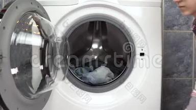 一位年轻妇女正积极地用洗衣机装衣服。 女人打开洗衣机扔衣服