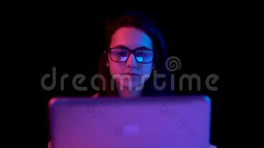 带着<strong>笔记本电脑</strong>的年轻女人。 一个女人在用<strong>笔记本电脑</strong>。 蓝色和红色的光落在黑色背景上的女人身上。