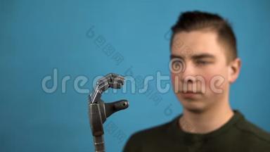 一个年轻人看着他的<strong>机械手臂</strong>。 赛博格在蓝色背景上用灰色的手挤压手指。