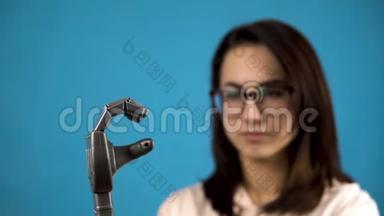 一个年轻的女人看着她的机械手臂。 赛博格在蓝色背景上用灰色的手挤压手指。