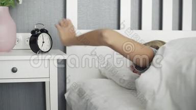 年轻漂亮的女人早上被闹钟吵醒了，但在停止闹钟后又恢复了睡眠。