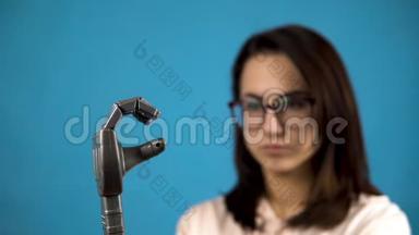 一个年轻的女人看着她的<strong>机械</strong>手臂。 赛博格在<strong>蓝色背景</strong>上用灰色的手挤压手指。