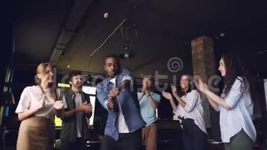 快乐的上班族非裔美国人在公司聚会上跳舞，而他的团队成员在鼓掌