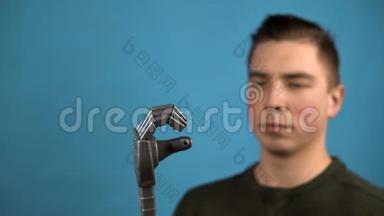 一个年轻人看着他的机械手臂。 赛博格在蓝色背景上用灰色的手挤压手指。