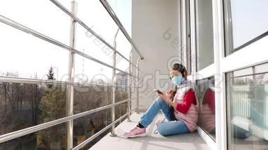 十几岁的女孩戴着面具和耳机，在智能<strong>手机</strong>上听音乐，在开放的阳台上。 <strong>春天</strong>阳光明媚的一天。 检疫