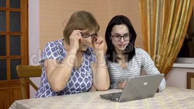女儿教妈妈如何使用笔记本电脑。 一个年轻的女人告诉她的老母亲在哪里点击电脑。 家庭