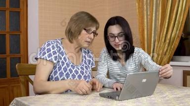女儿教妈妈如何使用笔记本电脑。 一个年轻的女人展示了如何打开她老母亲`笔记本电脑。 女人是