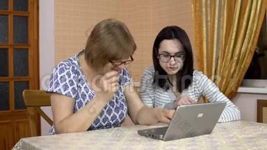 女儿教妈妈如何使用笔记本电脑。 一个年轻的女人告诉她的老母亲在哪里点击电脑。 那个女人
