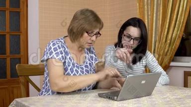 女儿教妈妈如何使用笔记本电脑。 一个年轻的女人<strong>告诉</strong>她的老母亲在哪里点击电脑。 家庭
