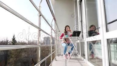 十几岁的女孩戴着耳机，在笔记本电脑上工作，在网上聊天，在开放的阳台上。 春天阳光明媚的一天。 远程学习