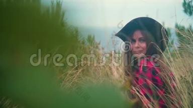一个长发女孩的肖像，穿着黑色和红色的衬衫，戴着牛仔帽，坐在干草里。
