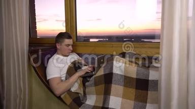 一个年轻人正在笔记本电脑上打字。 一个人躺在<strong>窗边</strong>的<strong>窗</strong>台上，手里拿着一台笔记本电脑。 在外面