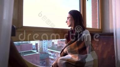 一个年轻的女人坐在窗边。 一个女人坐在铺着格子的窗台上，望着窗外