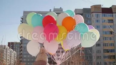 带着五颜六色气球束的女人走在城市街道的后景色。手拿<strong>彩球</strong>的年轻女子