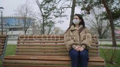 戴着口罩的漂亮女人坐在公园里的长凳上，在冠状病毒COVID-19流行<strong>时期</strong>