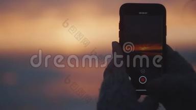 特写快乐旅游女人拍摄智能手机视频史诗粉红色日落天空风景在风海海岸慢动作。