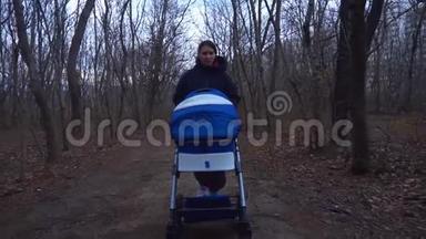 早春。 妈妈带着婴儿车在<strong>公园里散步</strong>。 一个穿着温暖夹克和帽子的女人在树林<strong>里</strong>卷着婴儿车