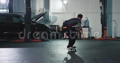 在大型汽车服务中心，穿着制服的机械师在工作场所玩滑板，玩得很开心