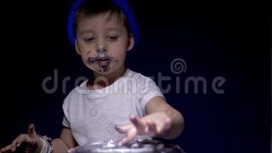 穿着蓝色帽子和白色t恤的小男孩吃一个喜庆的黑色蛋糕