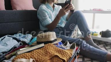 一个年轻女孩在旅行箱附近看着智能手机上的社交网络，和朋友聊天
