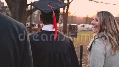 慢动作学院毕业生在日落时分与家人一起穿着帽子走路