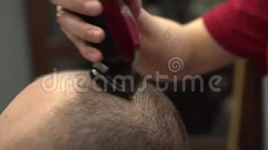 女人`手用电动剃须刀剪了几乎秃顶的男人。 在理发店，穿红色T恤的女孩给男生剪短发型。