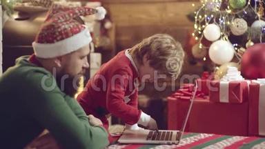 父亲和儿子在圣诞节玩得很开心。 可爱的小儿子和爸爸带着笔记本。 圣诞家庭。 快乐的父亲