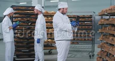在面包店行业，主要的面包师从一个新技术的平板电脑上拍下了其他货架上烘焙的新鲜面包的照片