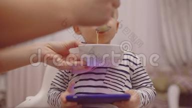 宝宝用手机小工具吃饭。有趣的孩子吃东西。在厨房吃早餐的小男孩。
