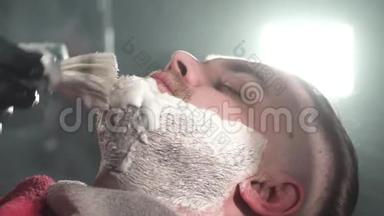 理发师用特殊的剃须膏涂在客户的脸上，并将用危险的剃须刀刮胡子。 光在背后闪耀