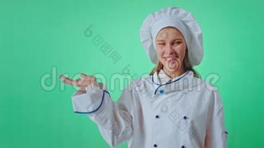 漂亮的女人面包师在一个绿色的工作室墙上，直视着相机，微笑着大，举起手，保持不变