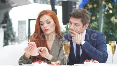 一对情侣在餐馆里浪漫约会。 浏览红发女孩智能手机上的在线菜单