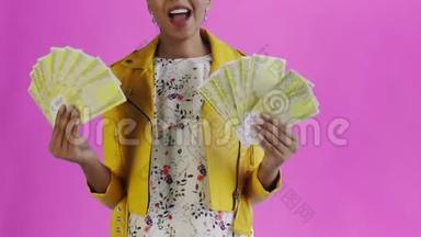 心满意足高兴兴奋的非洲裔美国妇女在粉色背景黄色夹克上炫耀金钱并说“上帝啊”