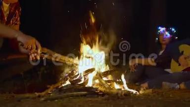 在露营旅行中，男人把木柴放在燃烧的篝火里。 游客燃烧篝火，用吉他<strong>唱歌</strong>