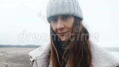 美丽的快乐女游客在镜头前微笑的特写镜头，在寒冷多风的冬季海边慢镜头下摆姿势