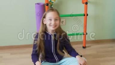 快乐的少女在<strong>学校体育馆</strong>里坐在地板上跳舞。 快乐少女摇着长发坐在地上