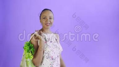 漂亮的美国黑人妇女手里拿着可重复使用的网状编织购物袋，里面有水果、蔬菜和蔬菜