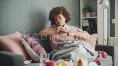 生病的非洲裔美国流感女孩躺在家里的沙发上。病了的年轻黑人妇女用感冒检查体温
