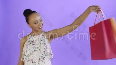 一位非洲裔<strong>美国</strong>妇女在摄影棚里摆着紫色背景的<strong>购物</strong>袋。快乐女人<strong>购物</strong>